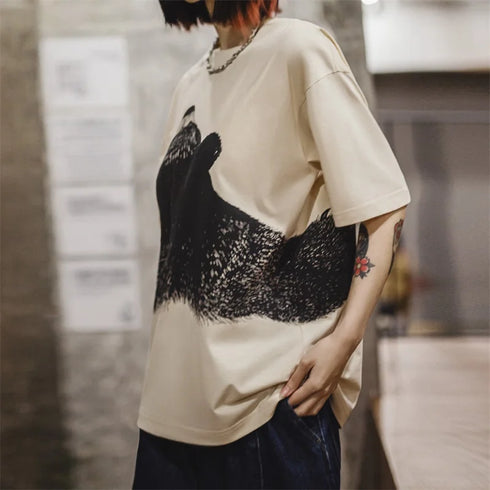 Person wearing a beige t-shirt with black graphic design in an indoor setting